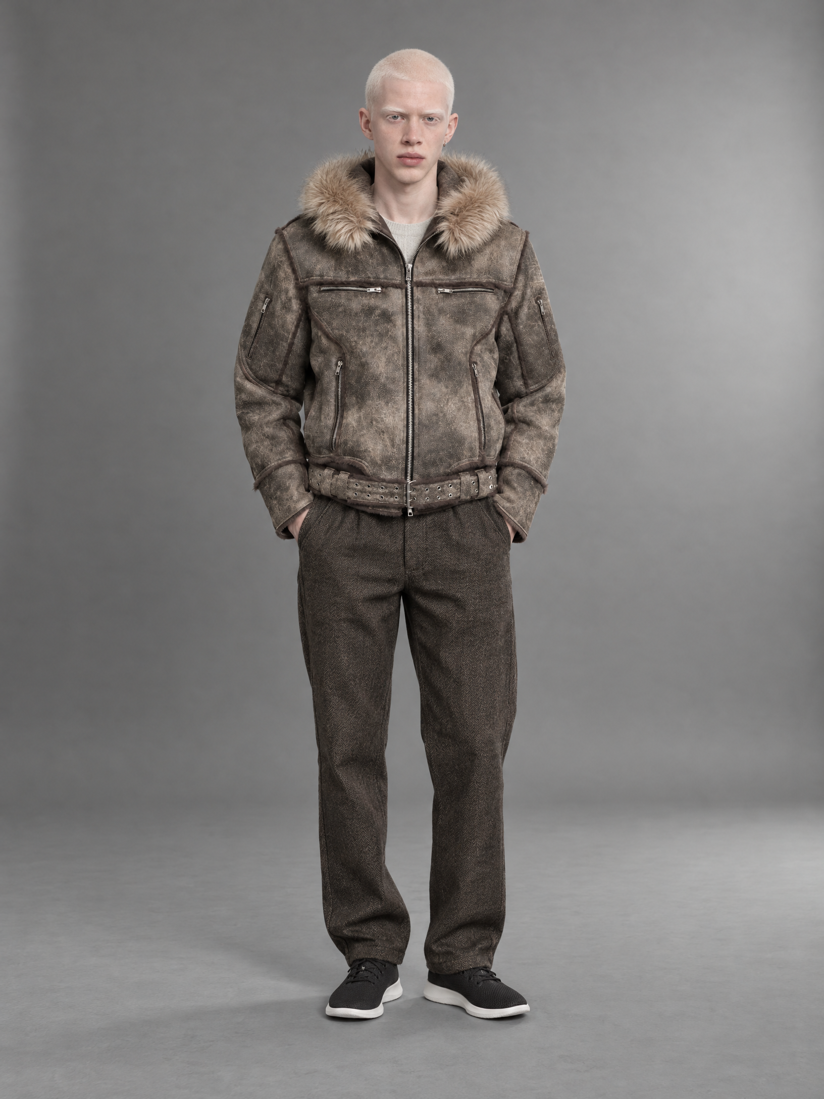 Fashion catalog photo. Reference images, in order: (1) the model's face and identity, keep his exact face, skin, hair and build: a man in his early twenties with albinism, white-pink skin, closely shaved white hair, white brows and lashes, pale blue eyes, small silver earring, slim build; (2) the footwear, The Allbirds Tree Runner is a breathable and lightweight sneaker made with responsibly sourced eucalyptus tree fiber that feels silky smooth and cool on your skin. These shoes are perfect for everyday, reproduce it exactly: cut, color, pattern, material and fit; (3) the bottom, The Carnegie Pant in Walnut Herringbone Wool, reproduce it exactly: cut, color, pattern, material and fit; (4) the top, Faded Sheepskin Jacket, reproduce it exactly: cut, color, pattern, material and fit; (5) the set, a mid-grey seamless paper sweep, soft directional light from the right, gentle gradient, use it as the whole scene. Compose one photograph of the model from image 1 wearing the footwear from image 2, the bottom from image 3, the top from image 4, standing straight facing the camera in a natural relaxed catalog pose, inside the set from image 5. Complete the outfit with plain neutral pieces only where a slot is missing. Full body visible head to toe, the figure about two thirds of the frame height, the set visible around his at real human scale (floor, furniture and doorways in proportion). Keep the set's own camera distance and perspective and place the model inside it at a natural distance, standing or sitting on its floor. Camera at chest height, normal 50mm perspective, no wide-angle distortion, no foreshortening toward the camera, hands and feet in normal proportion. Clean e-commerce catalog style: the whole outfit clearly visible and in focus, even flattering light, true garment colors, no props, calm expression. One real photograph, not a composite: the model is lit by the set's own light from the same direction and color temperature, casts a contact shadow on its floor, shares its depth of field, grain and white balance, with the edges of hair and clothes blending naturally. Sharp, true-to-life color. No text, no logos, no watermarks, no extra people.